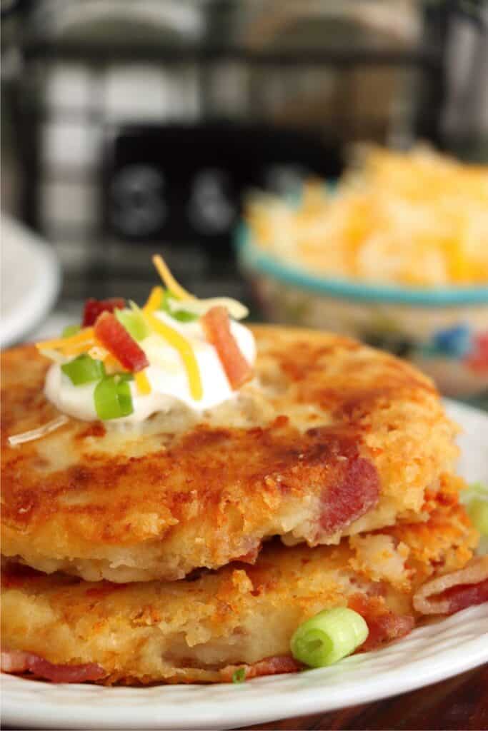 Closeup shot of two bacon and cheese leftover mashed potato patties stacked atop on another on plate. 