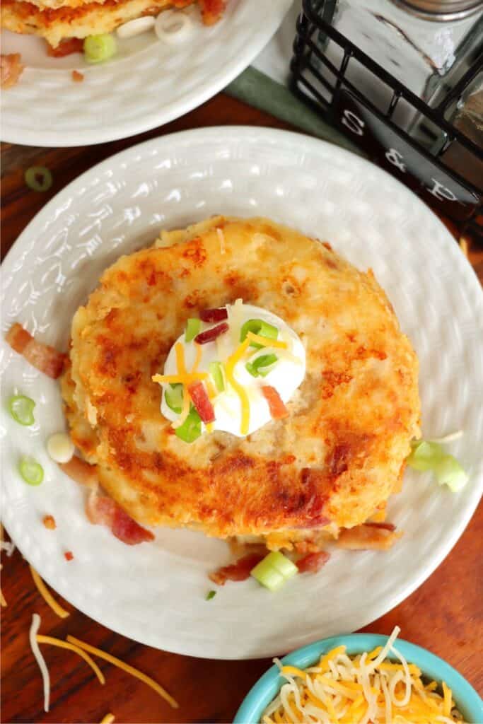 Overhead shot of bacon and cheese mashed potato patty topped with sour cream and green onions on plate. 