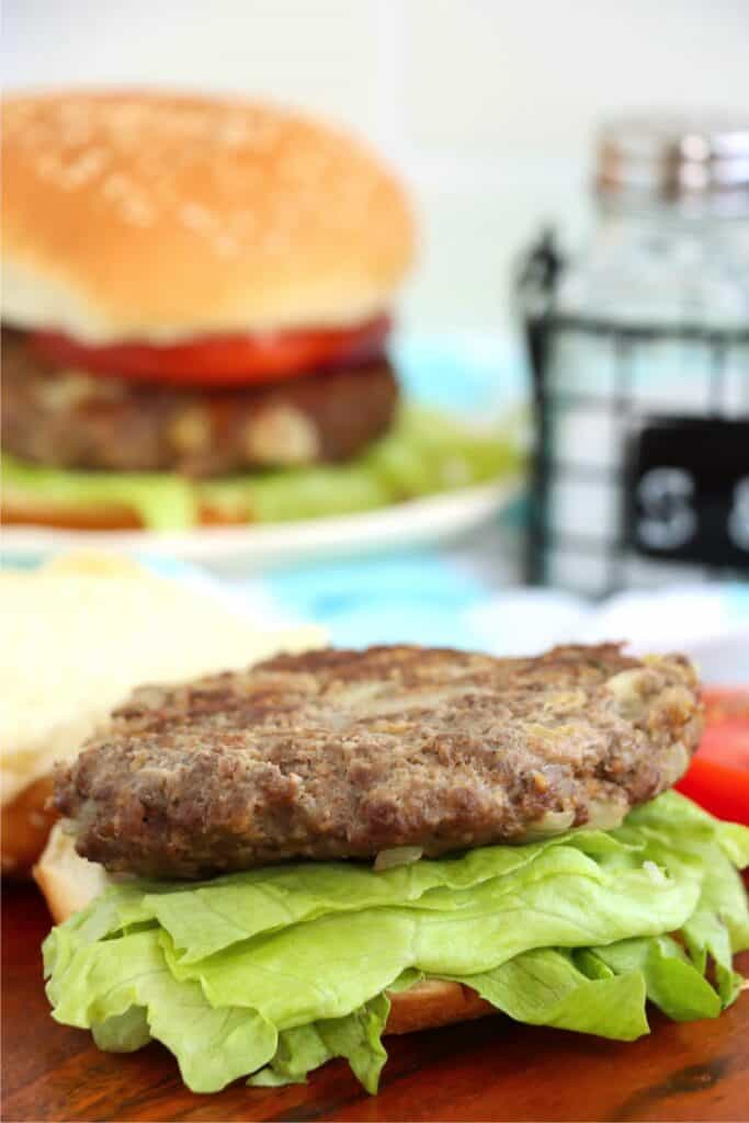 Closeup shot of classic American burger patty on bun with lettuce. 