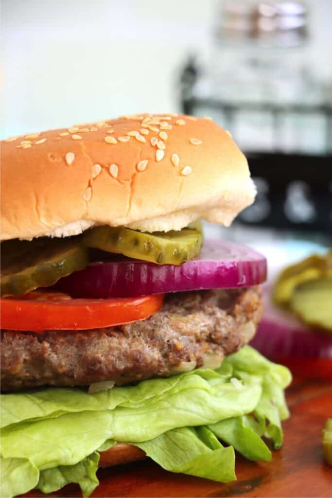 Closeup shot of classic American burger topped with lettuce, tomato, onions, and pickles. 