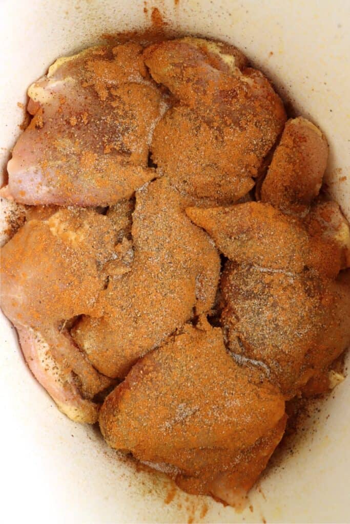 Overhead shot of uncooked chicken thighs topped with seasonings in slow cooker