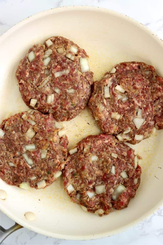 Overhead shot of four uncooked burgers in skillet