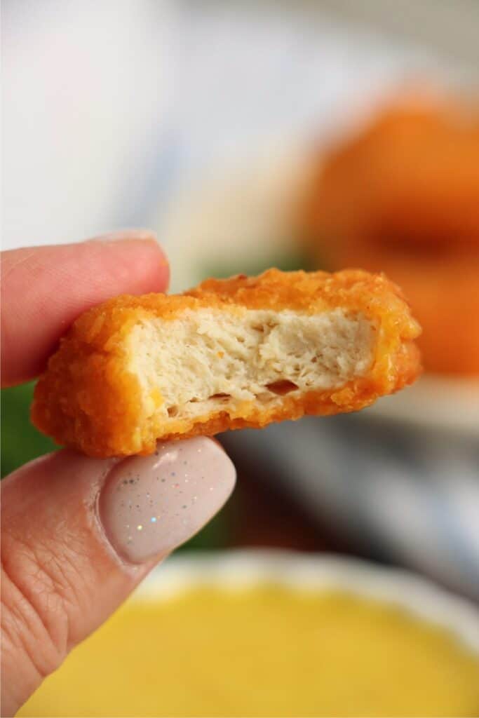 Closeup shot of a hand holding a Tyson air fryer chicken nugget with bite taken out. 
