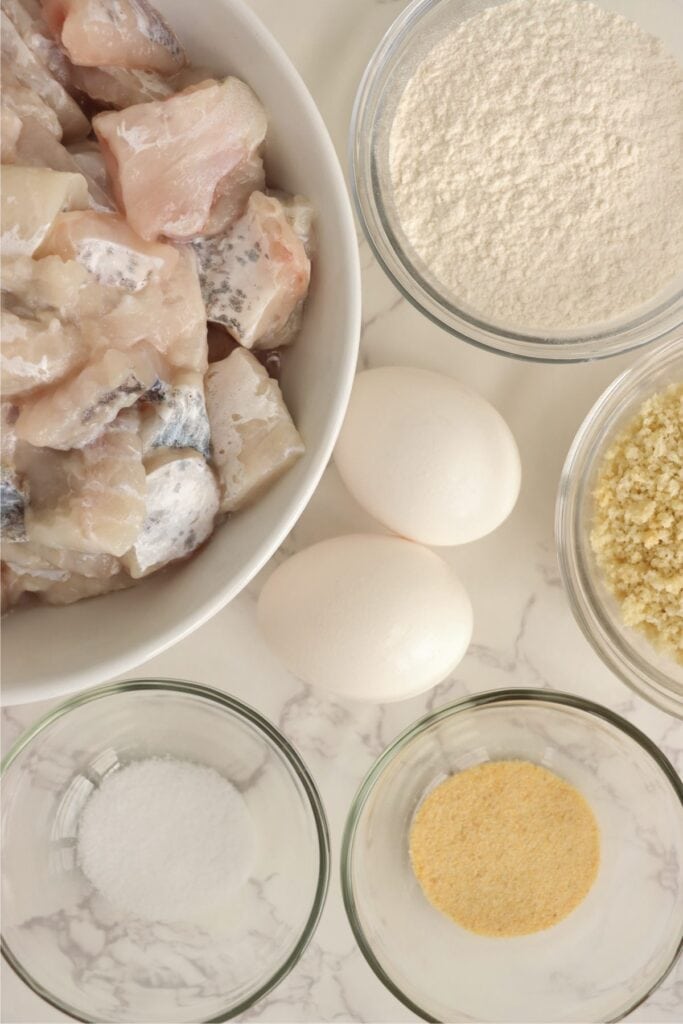 Overhead shot of individual air fryer catfish nuggets ingredients in bowls on table. 