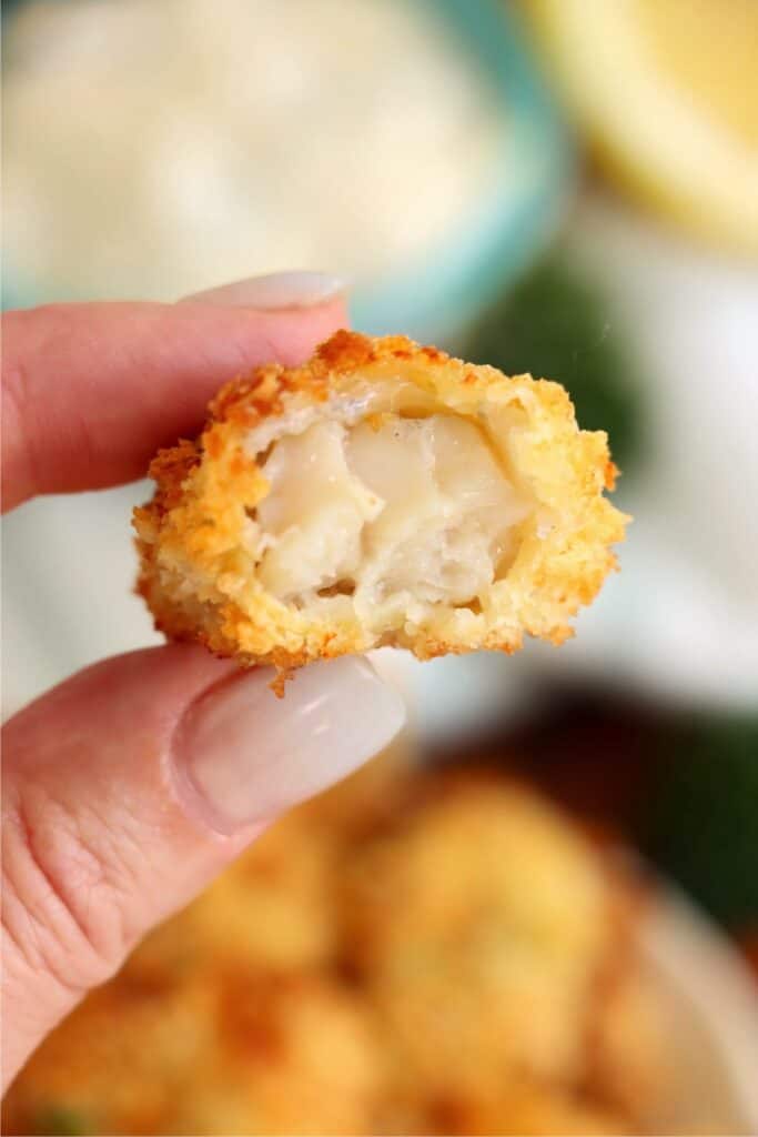 Closeup shot of hand holding an air fryer catfish nugget with bite taken out. 