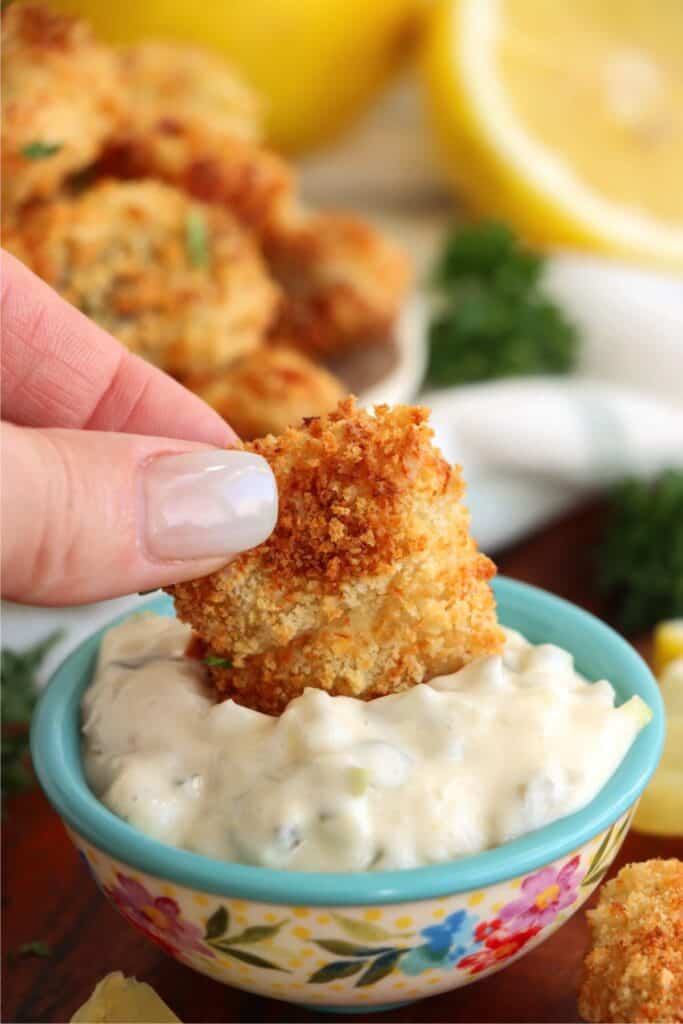 Closeup shot of air fryer catfish nugget being dipped in small bowl of tartar sauce. 