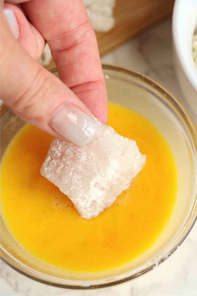 Closeup shot of floured catfish nugget being dipped in egg. 