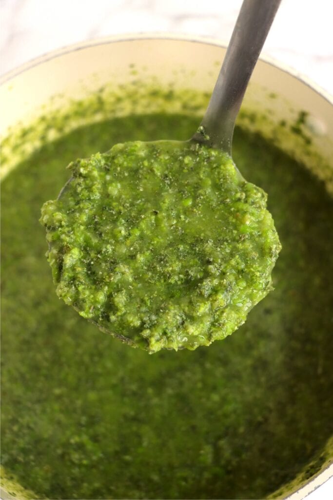 Closeup shot of ladel full of kale and spinach soup over potful of more soup.