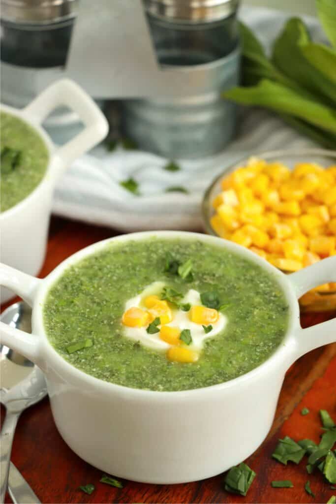 Closeup shot of bowlful of kale and spinach soup topped with sour cream and corn. 