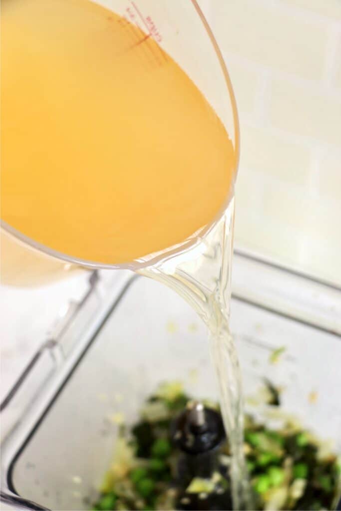 Chicken broth being poured into blender with vegetables. 