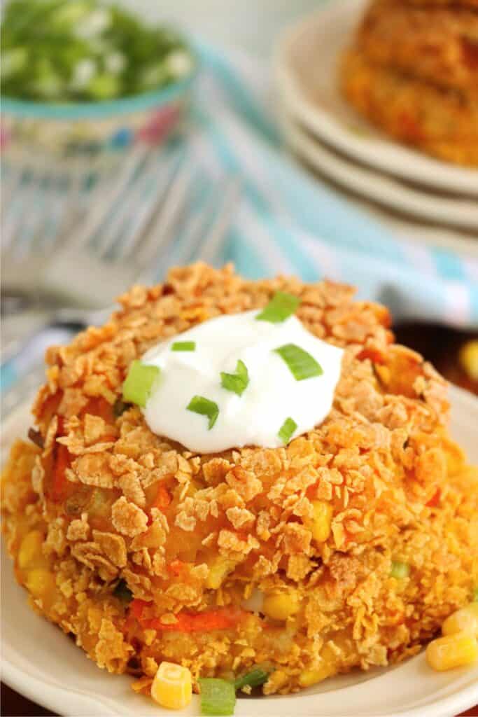 Two fried mashed potato and vegetable patties stacked atop one another on plate. 