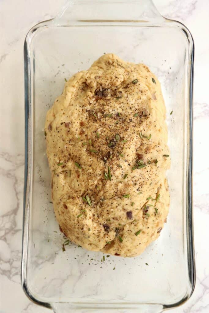 Overhead shot of sage bread dough topped with herbs in loaf pan