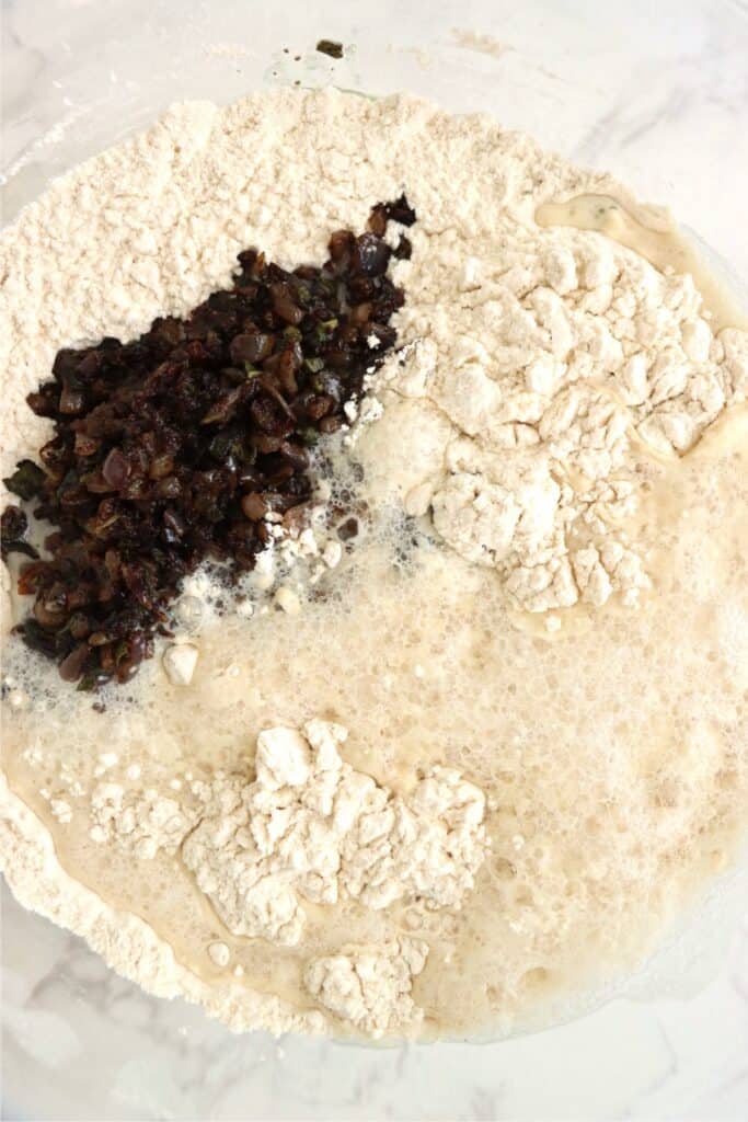 Overhead shot of onions, dry bread ingredients, and yeast mixture in bowl