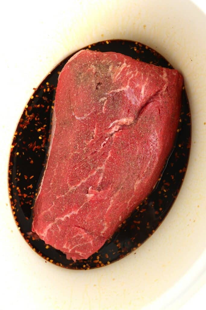 Overhead shot of seasoned roast in slow cooker with Asian sauce. 