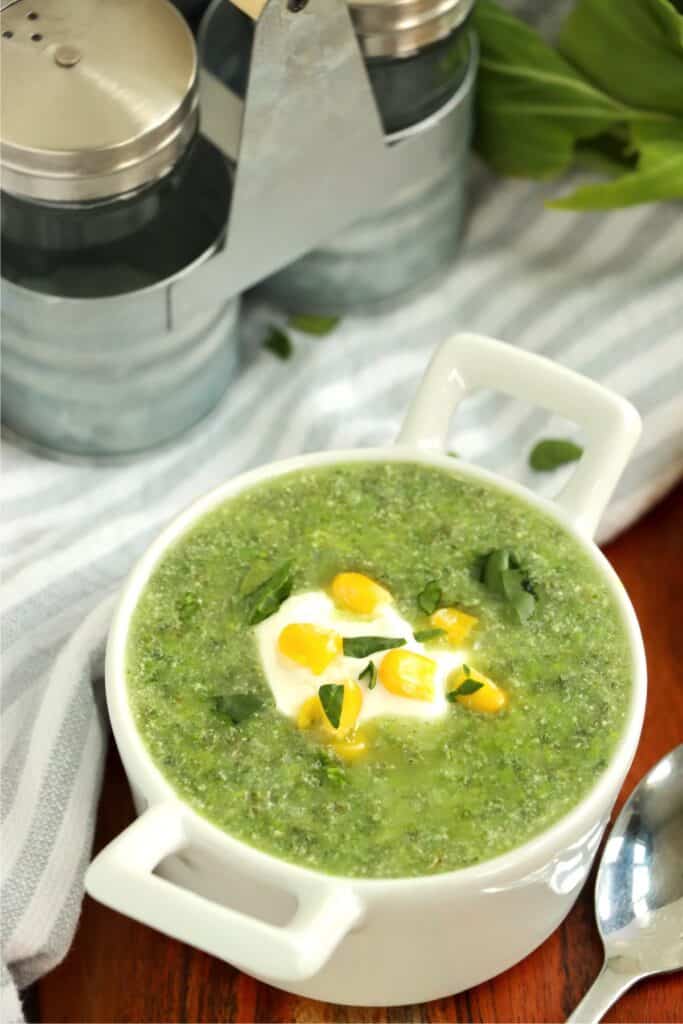 Bowlful of kale and spinach soup topped with sour cream and corn. 