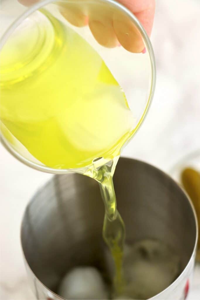 Closeup shot of pickle juice being poured into cocktail shaker filled with ice. 