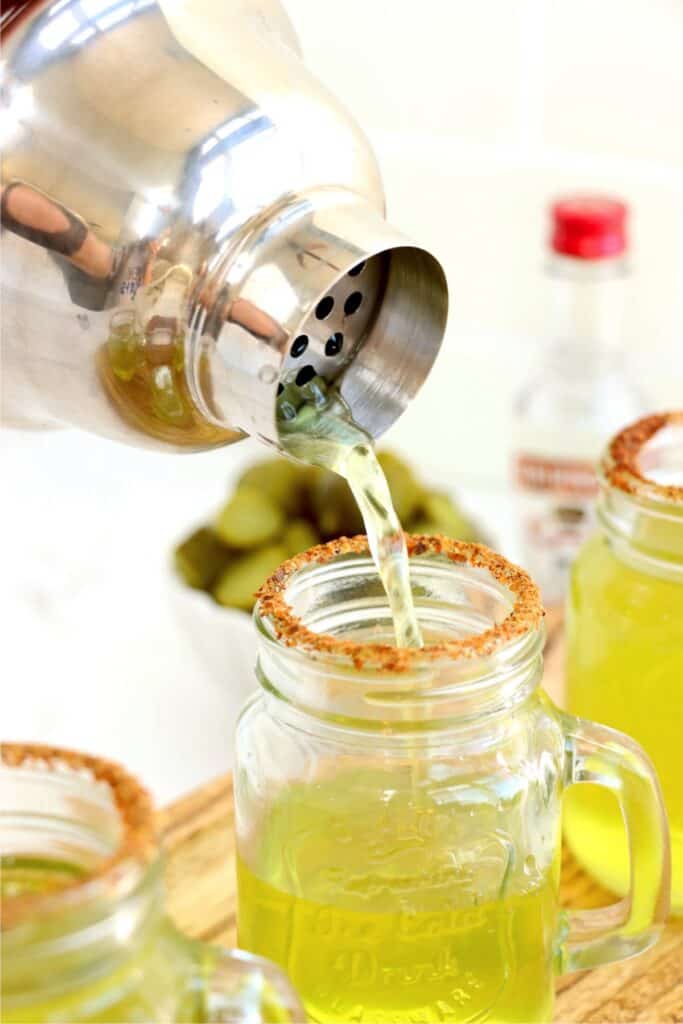 Dill pickle shot being poured into shot glass garnished with Tajin.