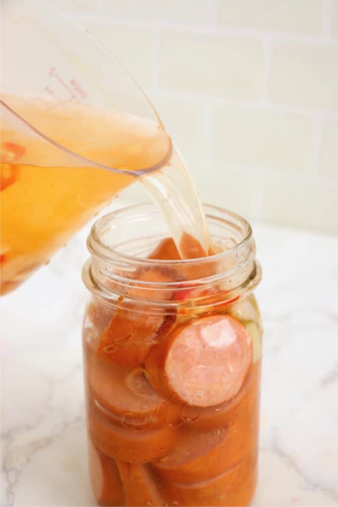 Pickling juice being poured into jar with sliced bologna. 