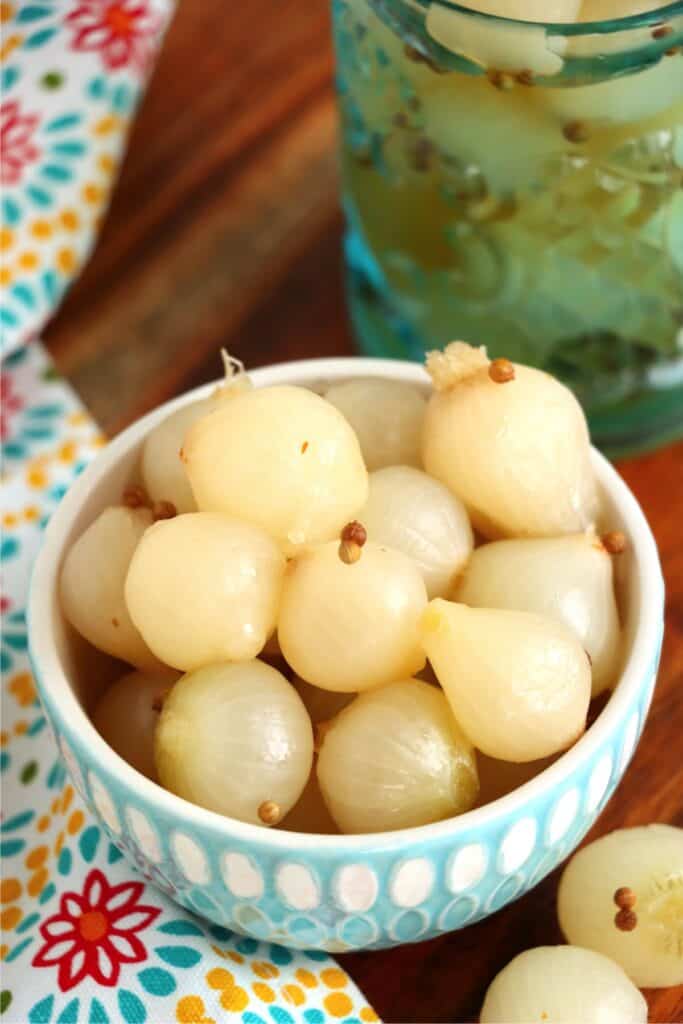 Closeup shot of bowlful of pickled pearl onions next to jarful of pickled pearl onions. 