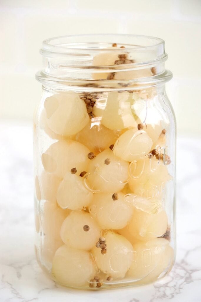 Closeup shot of jarful of pearl onions and coriander seeds.