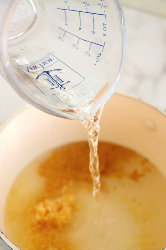 Closeup shot of vinegar being poured into potful of pickling spices. 