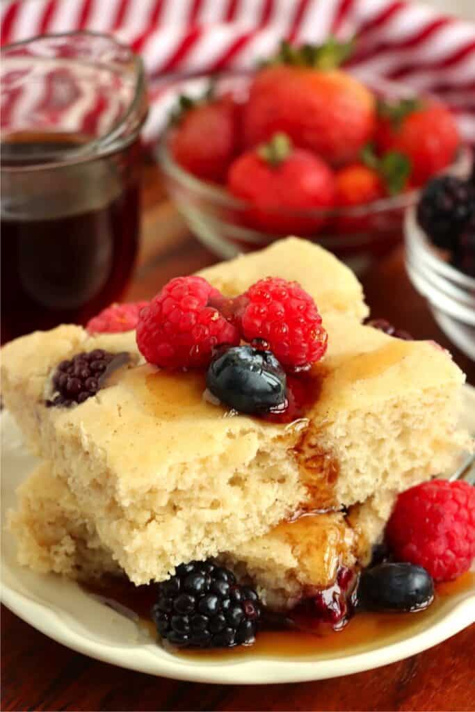 Closeup shot of two slices of sheet pan pancake topped with berries and syrup.