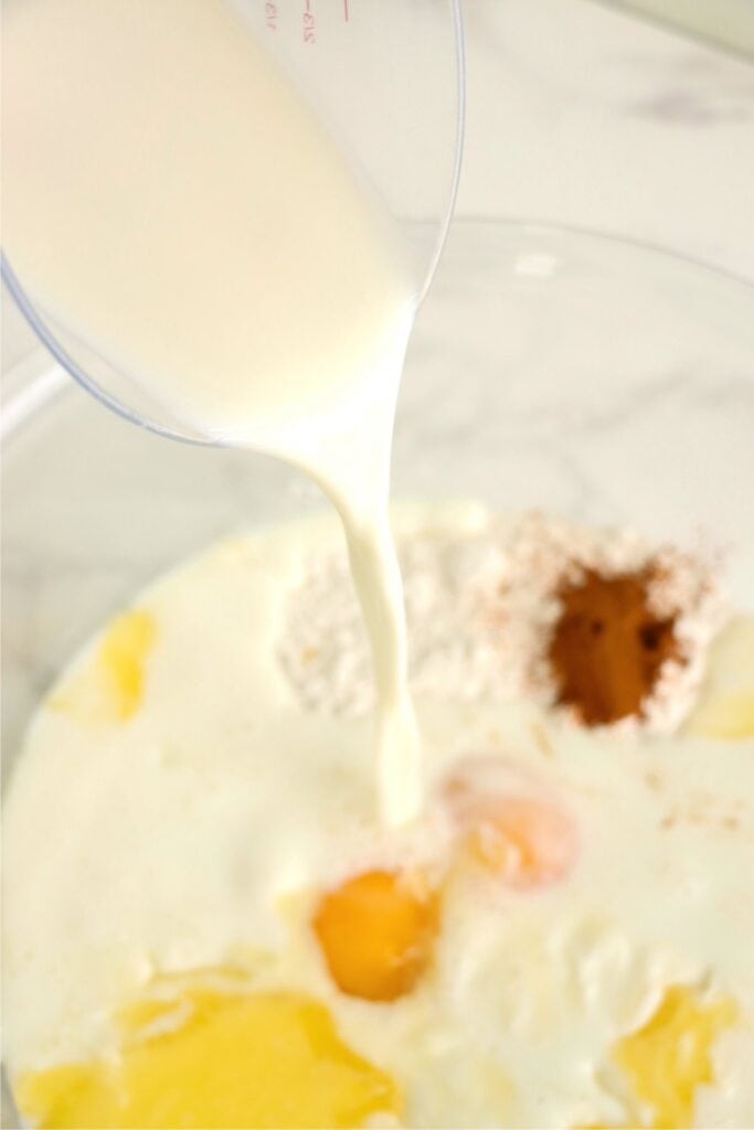 Closeup shot of milk being poured into mixing bowl with pancake batter ingredients. 