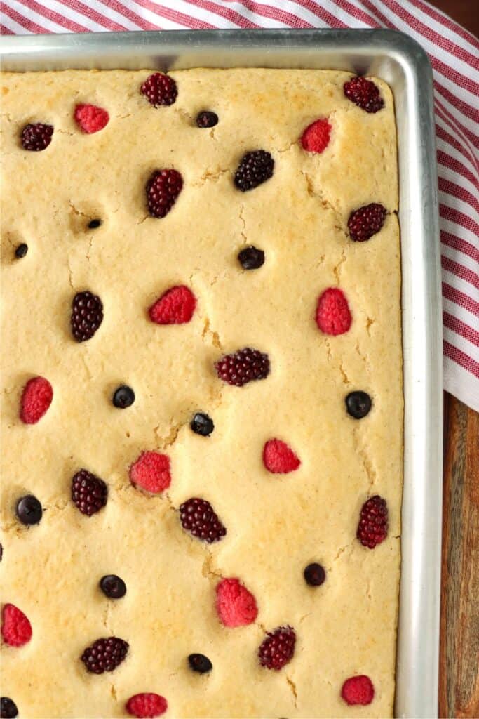 Overhead shot of golden brown mixed berry sheet pan pancake with mix in baking dish. 