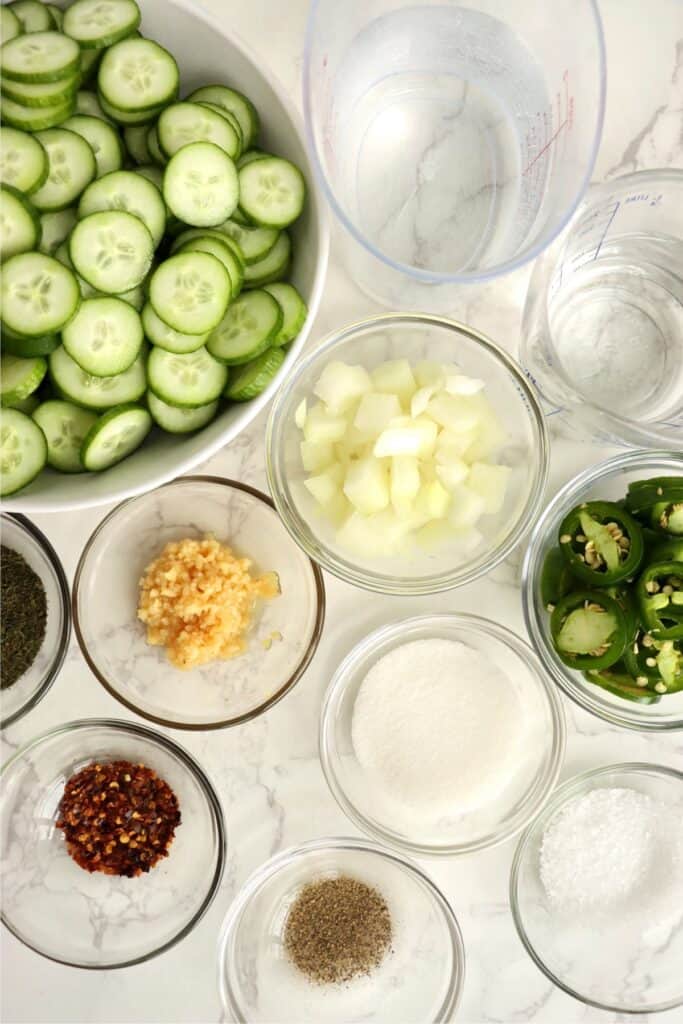 Overhead shot sweet and spicy pickle ingredients in individual bowls on table. 