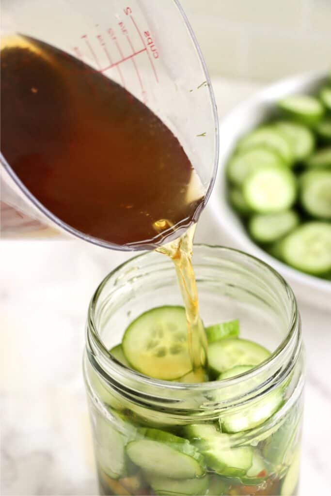 Pickling liquid being poured over cucumbers in jar. 