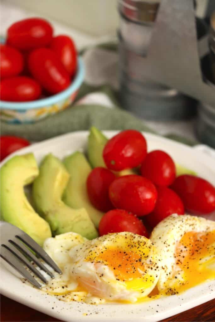 Closeup shot of plate with two air fryer soft boiled eggs, avocado slices, and grape tomatoes.