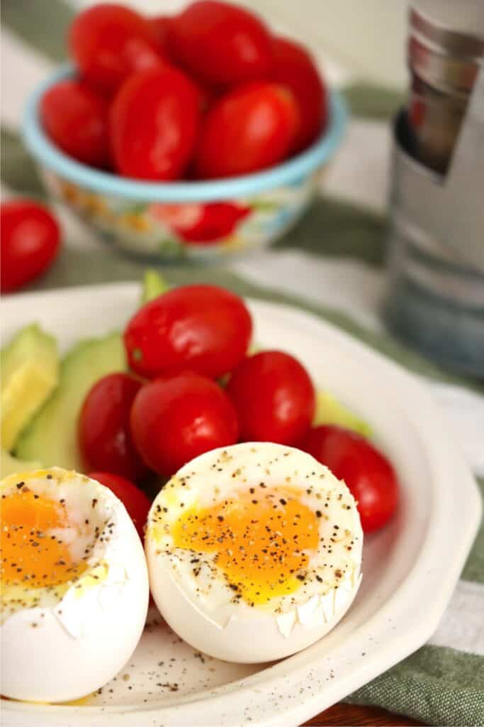 Closeup shot of two air fryer soft boiled eggs with grape tomatoes and avocado slices on plate.