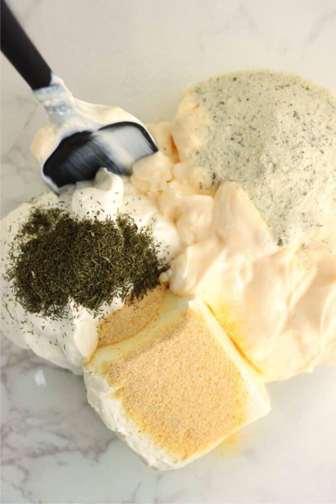 Closeup overhead shot of sour cream, mayo, cream cheese, and seasonings in bowl. 