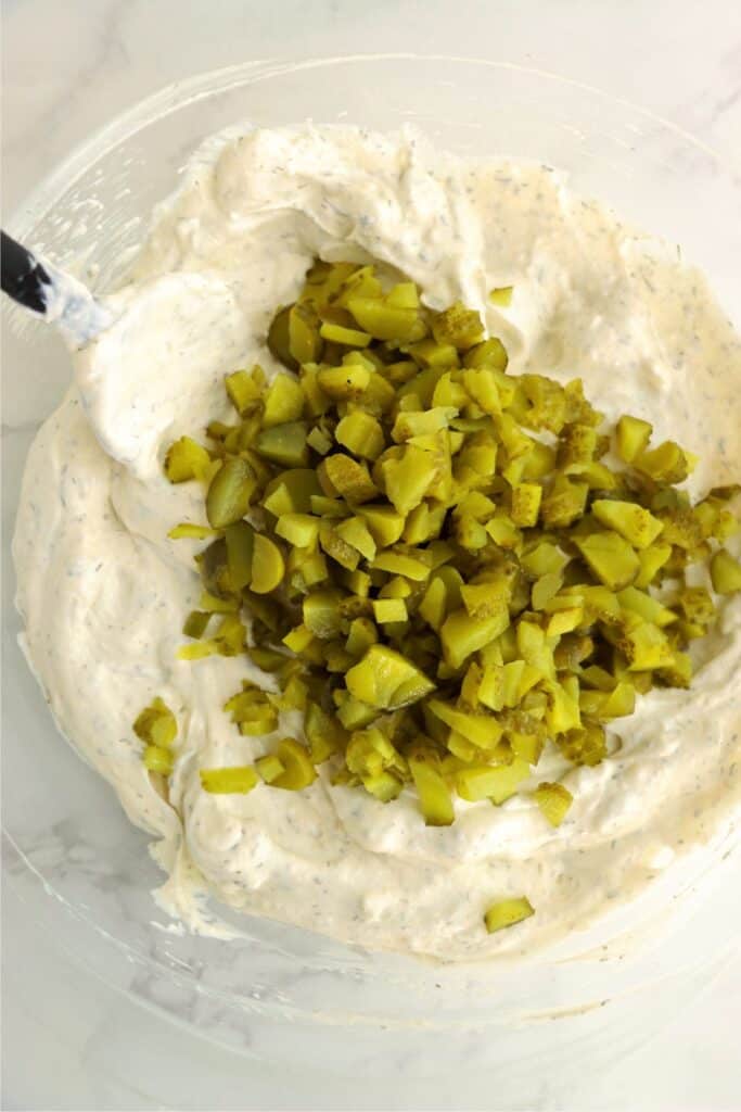 Overhead shot of dill pickles on top of creamy dip in bowl. 