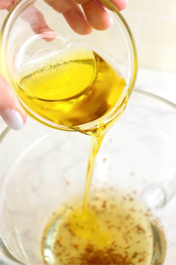 Closeup shot of oil being poured into glass mixing bowl.