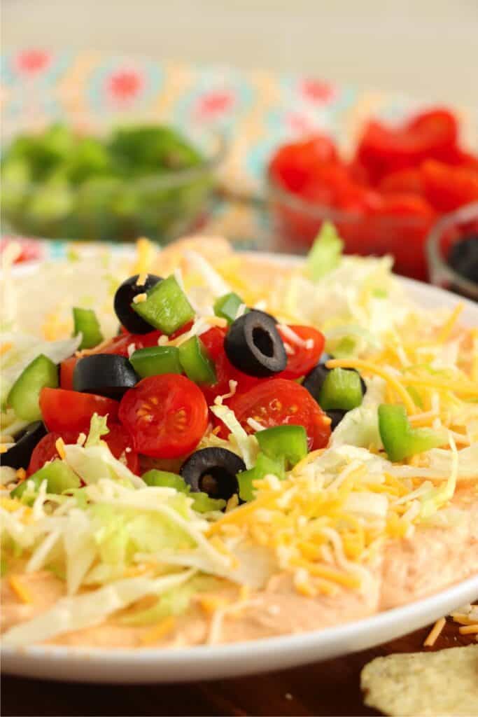 Closeup shot of fiesta taco dip topped with shredded cheese, tomatoes, bell peppers, lettuce, and olives. 