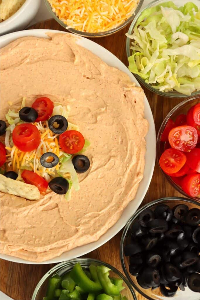 Closeup overhead shot of bowlful of 3 ingredient taco dip topped with shredded cheese, tomatoes, olives, and lettuce.