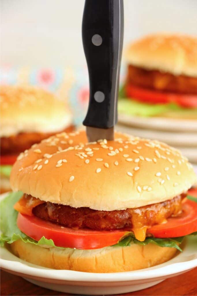 Closeup shot of knife stuck into the top of an air fryer chiken patty sandwich with cheese, tomato, and lettuce. 