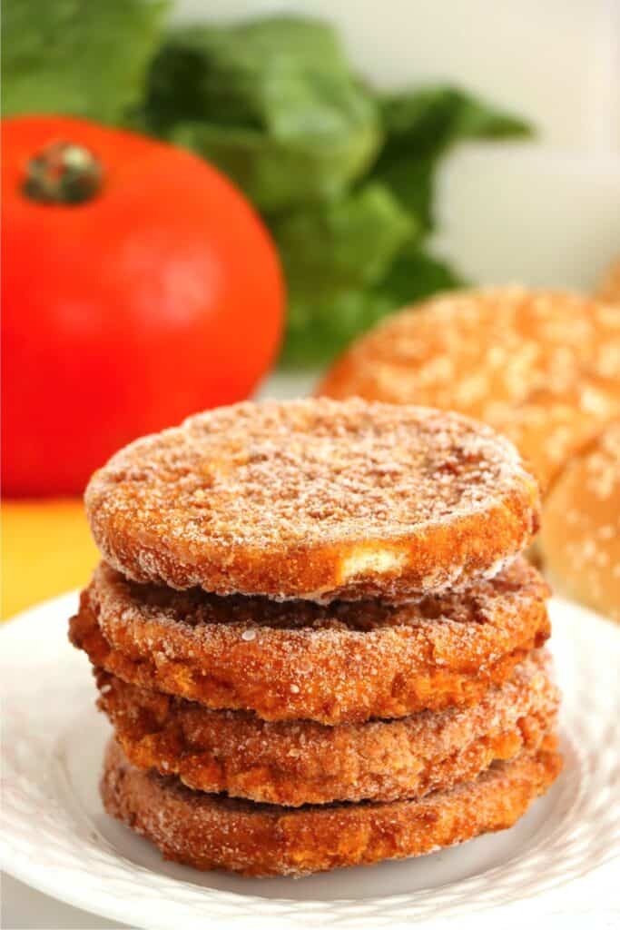 Closeup shoth of four frozen chicken patties stacked atop one another on plate. 