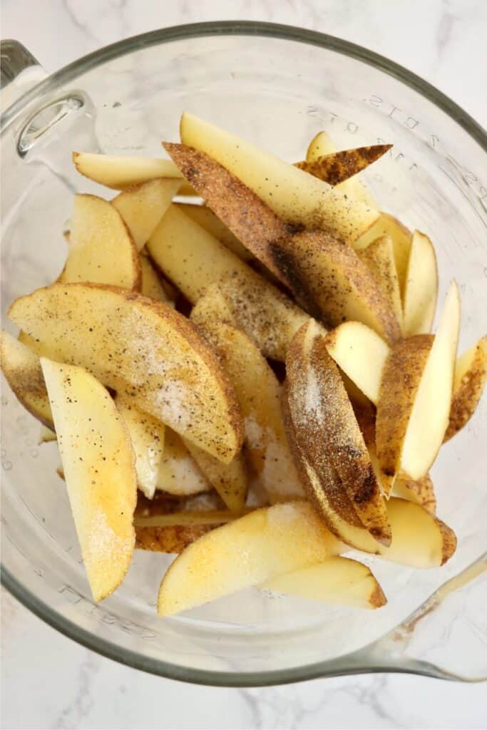 Overhead shot of potato wedges, seasonings, and oil in a large mixing bowl. 