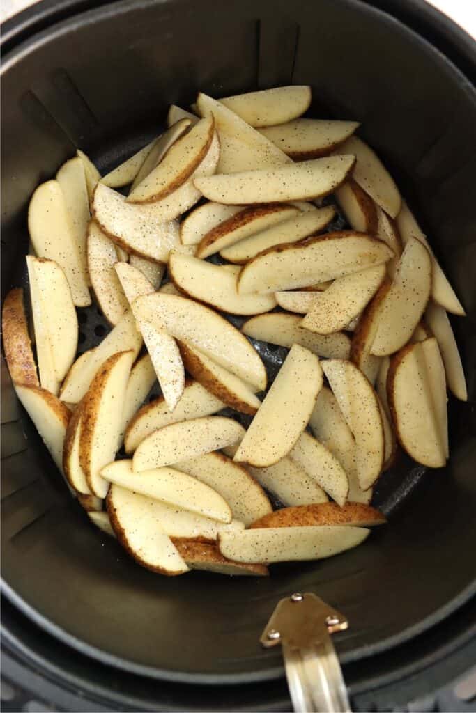 Overhead shot of seasoned potato wedges in air fryer basket. 