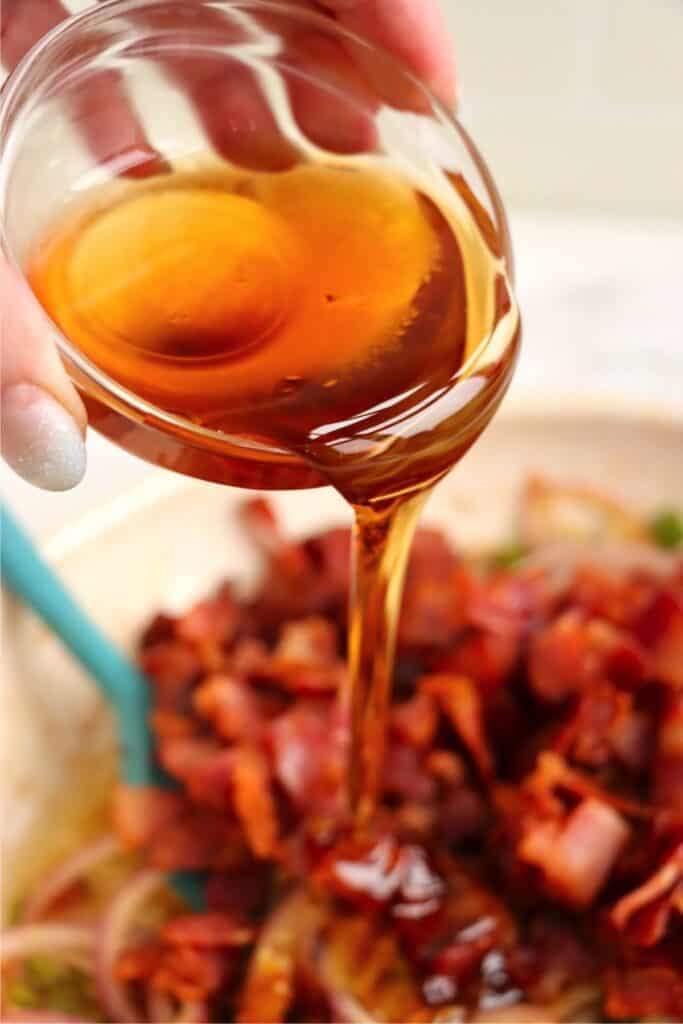 Closeup shot of maple syrup being poured into skillet filled with bacon and vegetables. 