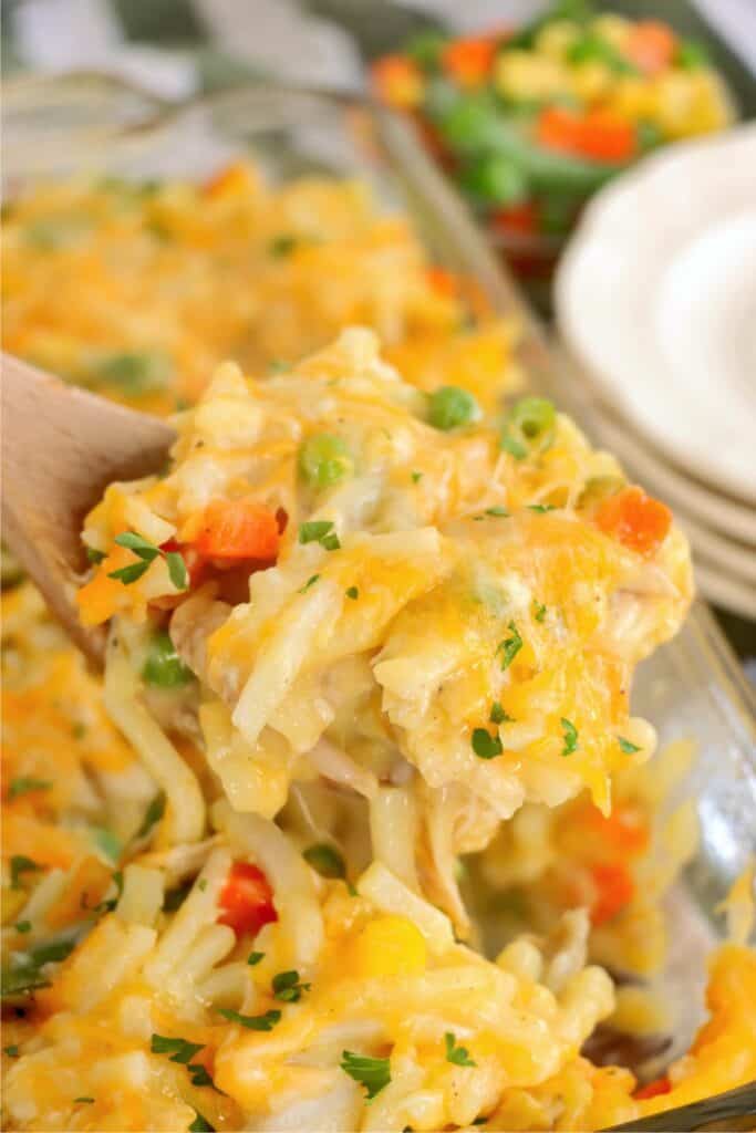 Closeup shot of wooden spoonful of cheesy chicken hash brown casserole. 