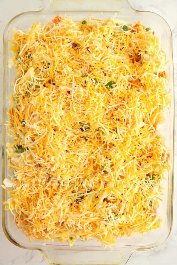 Overhead shot of baking dish full of unbaked casserole topped with cheese.