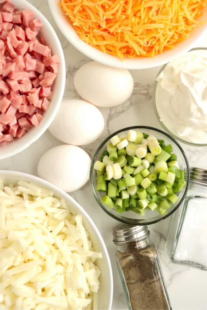 Overhead shot of individual ham and cheese hash brown casserole ingredients in bowls on table