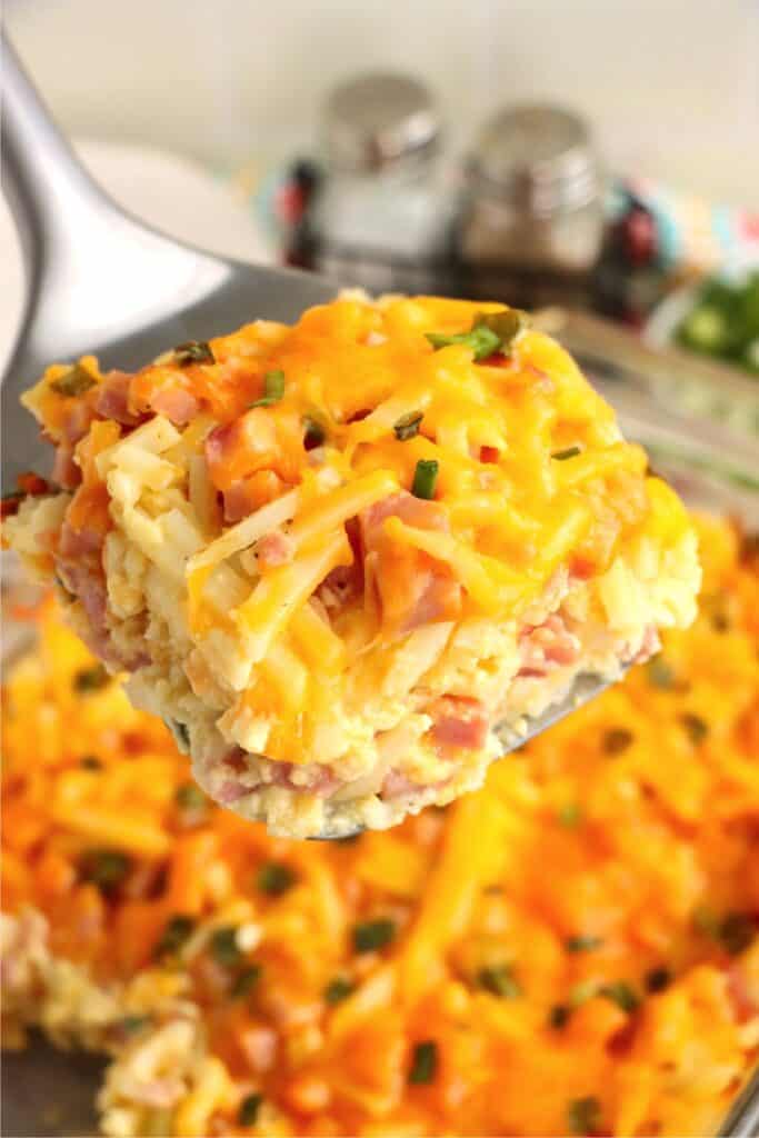 Closeup shot of spatula with slice of ham and cheese hash brown casserole. 