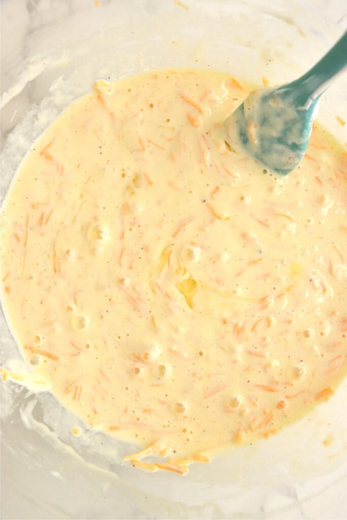 Overhead shot of sour cream, eggs, salt, pepper, and shredded cheese in mixing bowl. 