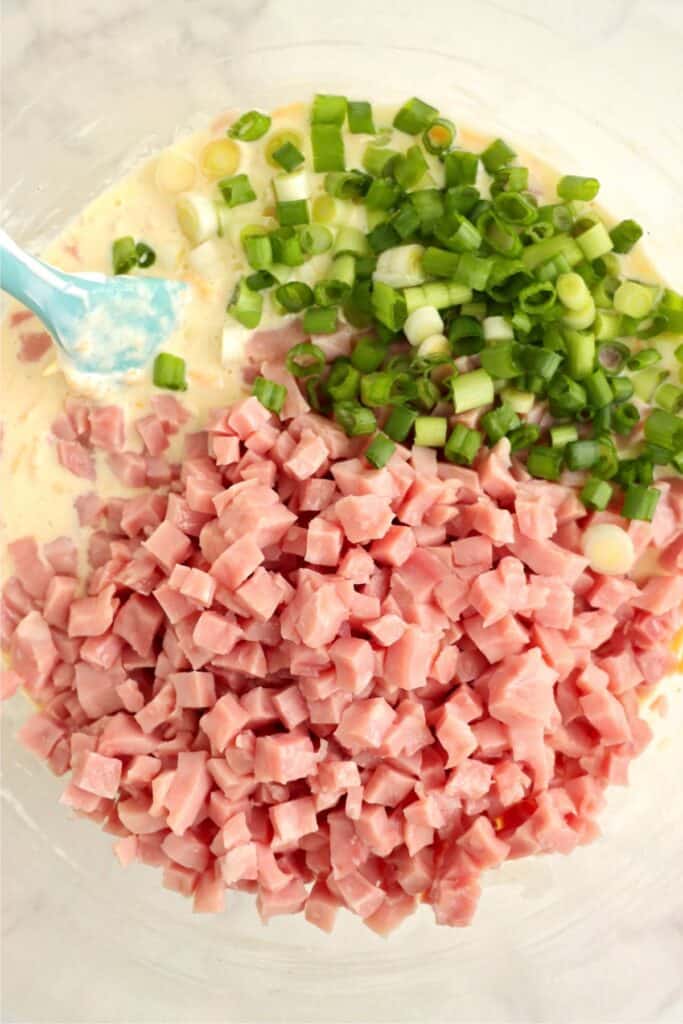 Overhead shot of eggs, sour cream, cheese, ham, and green peppers in bowl. 