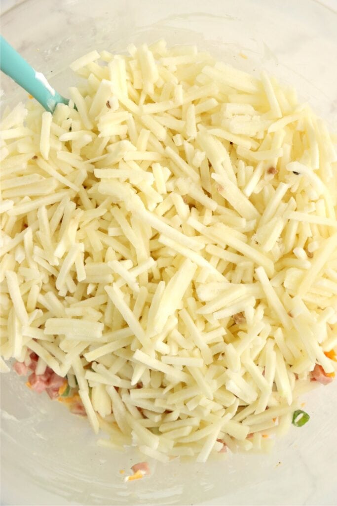 Closeup shot of frozen hash browns on top of the rest of the hash brown ingredients in mixing bowl. 