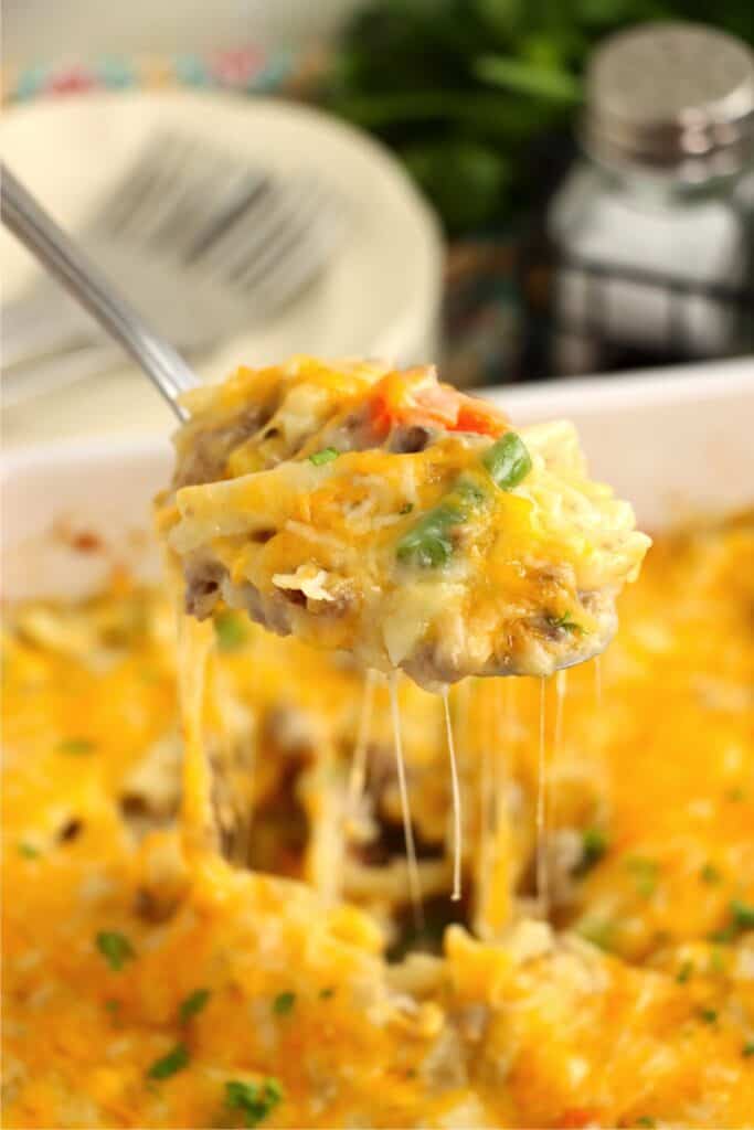 Closeup shot of spoonful of ground beef and hash brown casserole over dish withmore casserole. 